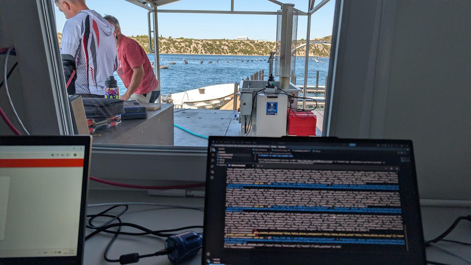 Laptops running code in the office on the Smart Mussel Farm platform, with the sea and Šibenik Bridge behind